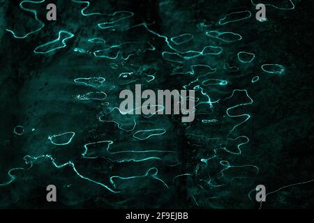 Waves of light reflections on dark background. Abstract curves lines  of fluorescent light on ice surface. Dark  background with organic, liquid light Stock Photo