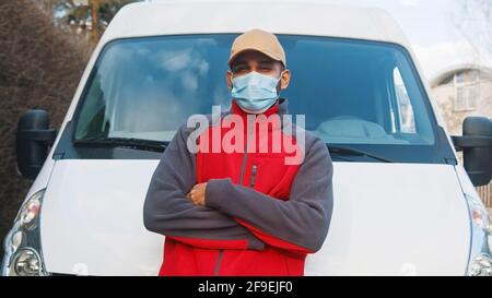 Delivery man with face mask and crossed hands standing in front of the van. High quality photo Stock Photo