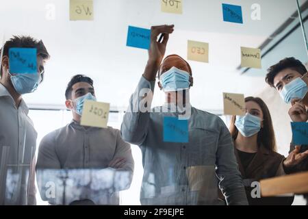 Businesspeople having meeting using sticky notes on glass wall Stock Photo