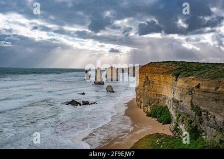 Sun rays shining through stormy clouds on the Twelve Apostles rock formations on the Great Ocean Road in Victoria, Australia Stock Photo