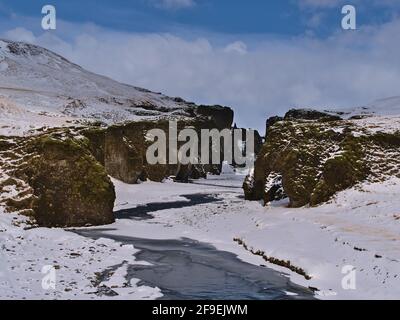 Stunning view of the entrance of famous gorge Fjaðrárgljúfur in the south of Iceland near ring road with snow-covered rocks, steep cliffs and  river. Stock Photo