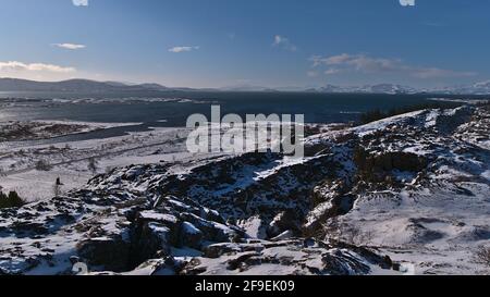 Stunning panoramic view of blue colored lake Þingvallavatn, largest natural lake of Iceland, and rugged, snow-covered mountains viewed from Þingvellir. Stock Photo