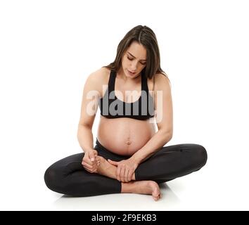 Pregnant woman massaging her inflamed ankles, isolated on white background Stock Photo