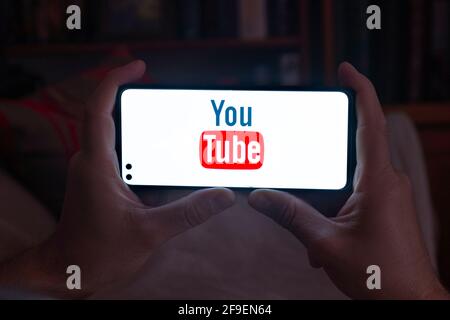 Spain. 04, 18, 2021. Close-up of a man holding a smartphone with the Youtube home screen on his sofa at night Stock Photo