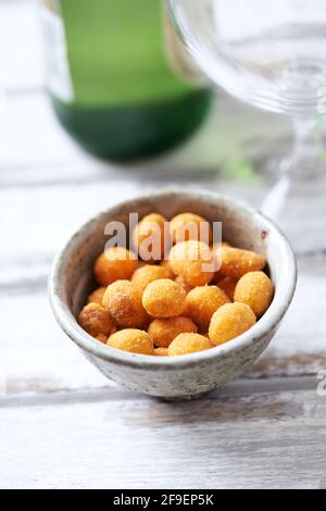 Spicy nuts in a ceramic dish; a bottle of beer in background. Bright wooden background. Close up. Stock Photo
