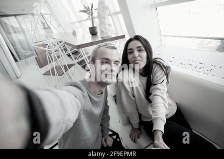 Man and woman taking selfie. Couple having good time in coffee shop. Man holding camera or smartphone when woman pose and showing tongue. Coffee house Stock Photo