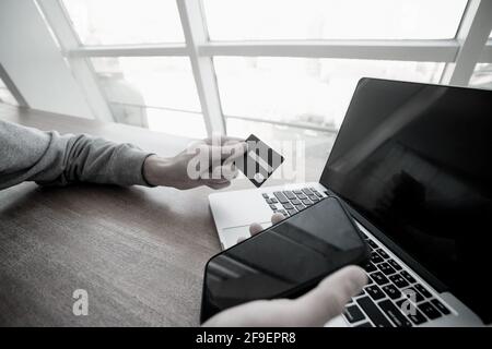 Male hands hold smartphone and credit card with laptop on background. Don't enter your credit card details on suspicious sites. Man using card to make Stock Photo