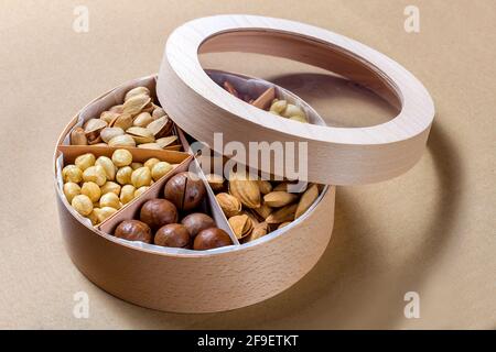 wooden round gift box with the lid open and set of different types of nuts for a healthy diet of vegetarians on paper eco craft background, nobody. Stock Photo