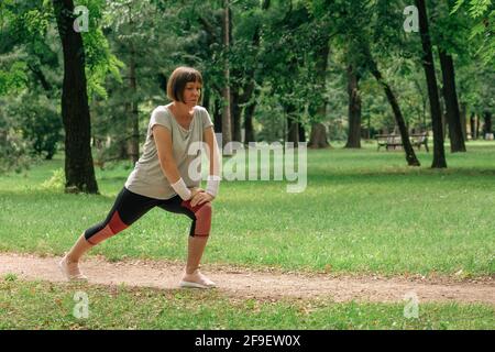 Female jogger stretching muscles and warming up for running exercise in park, selective focus Stock Photo
