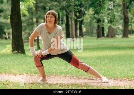 Female jogger stretching muscles and warming up for running exercise in park, selective focus Stock Photo