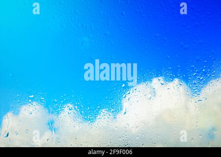 Bright blue sky with white clouds behind rain drenched glass Stock Photo