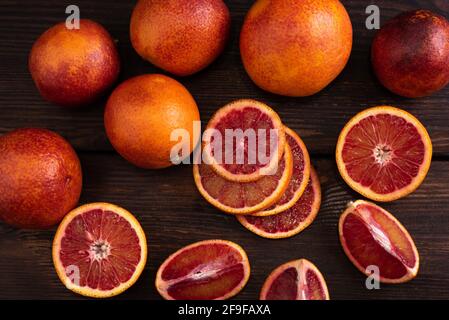 Background of whole and cut blood oranges on dark wooden board, close up. Stock Photo