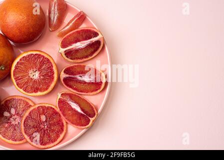 Plate with juicy sliced blood oranges on a pink background, healthy food, top view, close up. Stock Photo