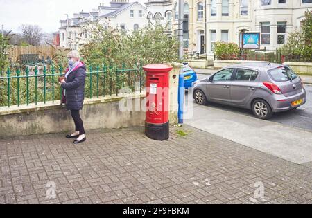 An older woman queuing outside a post office during the covid times with newly painted George VI postbox outside Stock Photo