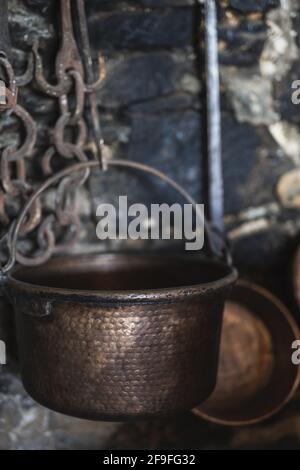 A vertical closeup shot of an old copper pot with rusty chains and aged brick wall in the background Stock Photo