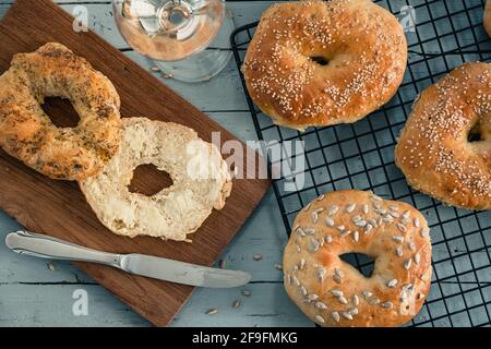 Homemade bagels on a cooling rack on grey wood, one with butter on a wooden board, glass of wine. Top view. Stock Photo