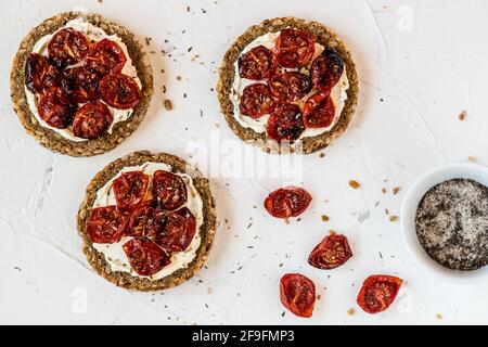 Round slices of wholemeal bread with grilled tomatoes on cream cheese. Top view. Stock Photo