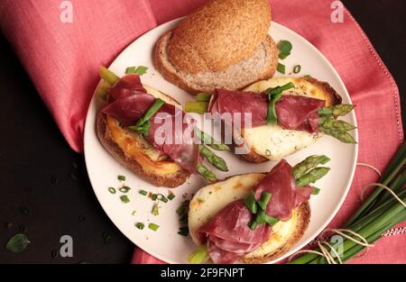 Bresaola and asparagus rolls with cheese and toasted bread on dark background. Healthy food. View from top. Stock Photo