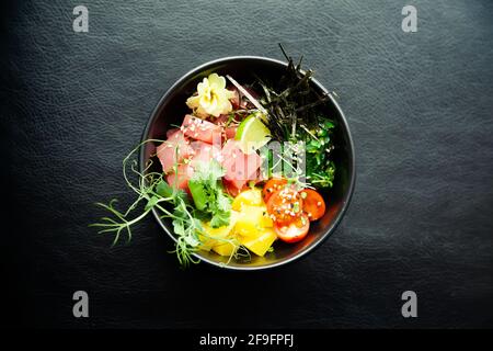 Poke salad with tuna in a bowl. Ingredients fresh tuna, cherry tomatoes, marinated seaweed, rice, takuan, Ponzu sauce, Teriyaki sauce, nori, sesame Stock Photo