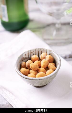 Spicy nuts in a ceramic dish; a bottle of beer in background. Bright wooden background. Close up. Stock Photo