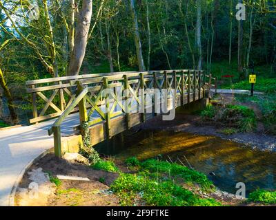 Timber footbridge over the Skelton Beck stream in the Saltburn Valley Gardens North Yorkshire England with a yellow and black warning sign for social Stock Photo