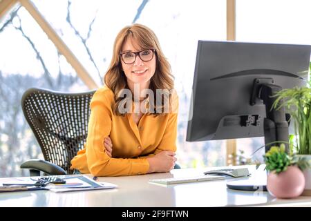 Shot of happy mature businesswoman sitting at office desk while working on computer at the office. Stock Photo