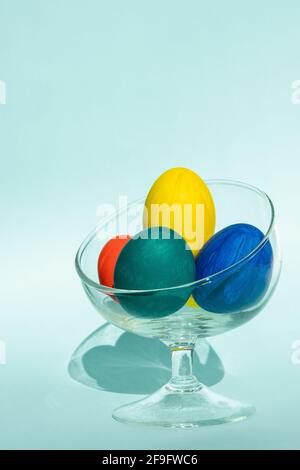 Hand-painted colorful Easter eggs in a transparent glass vase against a light blue background, vertical frame, copy space, close-up. Happy Easter conc Stock Photo
