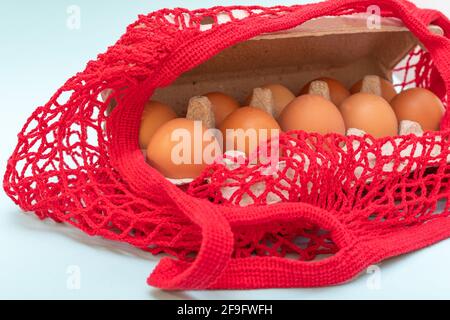 Easter shopping concept. Buying eggs. Close-up of natural raw eggs in a cardboard egg box and in a red string bag. Stock Photo