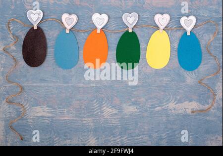 Easter colorful handmade greeting card made of Easter eggs cut out of their multi-colored paper hanging on a rope on clothespins on a blue wooden back Stock Photo