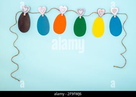 Easter colorful handmade greeting card made of Easter eggs cut out of their multi-colored paper hanging on a rope on clothespins on a blue background, Stock Photo