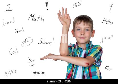 A smart, cute boy raises his hand to answer in class. Happy child against a white board with inscriptions. Education concept, concept back to school Stock Photo