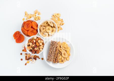 Granola bar and different types of nuts and dried fruits on a white background. Top view, copy space. Stock Photo