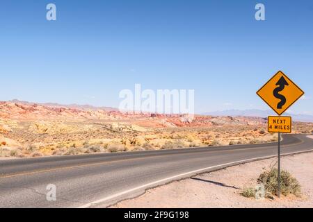 A Curve and Turn Road for the Next 4 Miles Sign by the Highway with Red Aztec Sandstone and rock formation at Valley of Fire State Park in Nevada Stock Photo