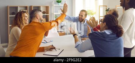 Happy business team clapping hands while two colleagues giving high five gesture Stock Photo