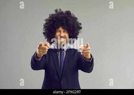 Happy smiling bearded man in crazy curly wig pointing index fingers at camera Stock Photo