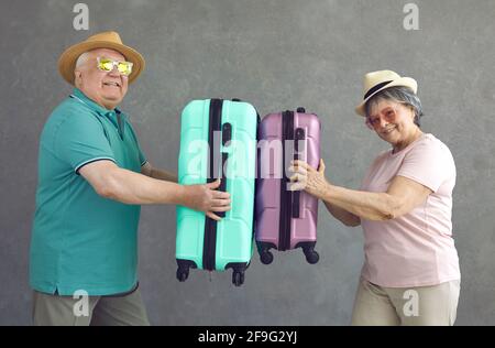 Funny active senior married couple of tourists with bright suitcases in hands on a gray background. Stock Photo
