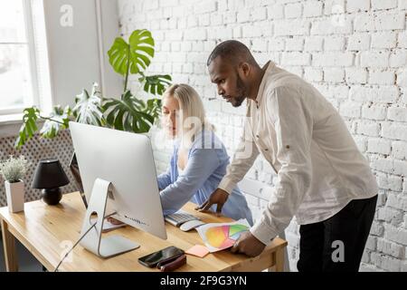 Serious mixed race colleagues using computer, working on report, learning financial graphs. Focused business partners developing new project Stock Photo