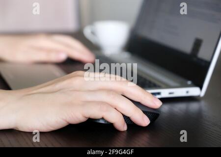Female hands on laptop keyboard and computer mouse. Woman works with docs sitting at the wooden desk Stock Photo