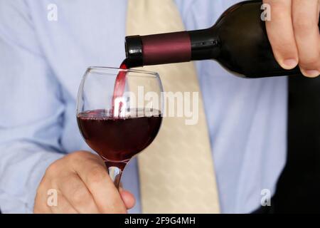 Man in business clothes pouring red wine in a glass from the bottle. Corporate party in office, romantic dinner in a restaurant Stock Photo