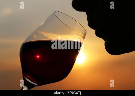 Man drinking red wine, silhouette of face with glass at sunset. Enjoying alcohol, romantic dinner at the resort, luxury life Stock Photo