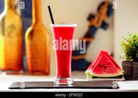 Freshly squeezed watermelon juice on a black stand and three oranges next to it. Stock Photo