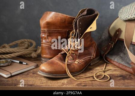 old leather travel vintage boots shoes and bag at wooden table, with wall background texture Stock Photo
