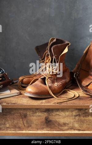 old leather travel vintage boots shoes and bag at wooden table, with wall background texture Stock Photo