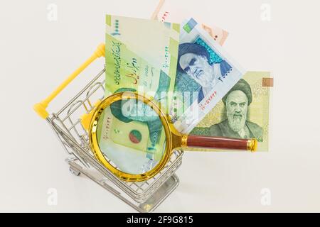 A miniature shopping cart with Iranian currency and a magnifying glass. Economic and business concept, rising inflation and the country's economic ups Stock Photo