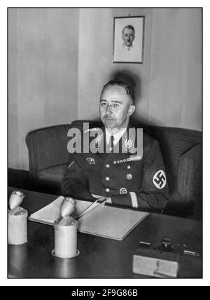WW2 1939 Heinrich Himmler in his Nazi uniform at his Berlin desk making a propaganda radio broadcast to the Nazi Germany population. Portrait of Fuhrer Adolf Hitler behind Stock Photo