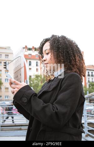 young black woman with curly hair using a cell phone in the city. Stock Photo