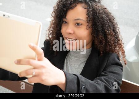 curly-haired woman holds up a tablet while making a video call Stock Photo