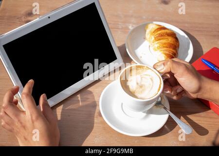 Person without identity drinking a coffee while using his tablet. top view. Stock Photo