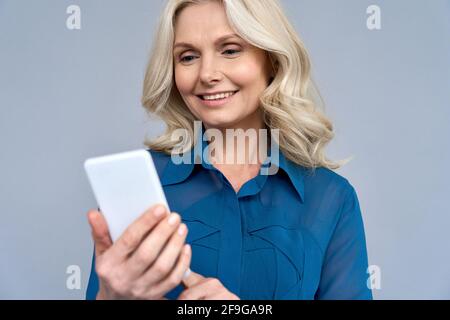 Shot of senior 50s aged blonde female manager using phone isolated on gray Stock Photo