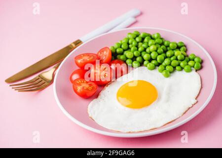 Sunny side up fried egg with green peas on a pink background, closeup view. Breakfast food Stock Photo
